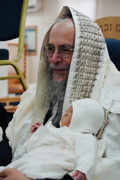 צילום ברית מילה - תינוק בטלית בזרועות הסבא